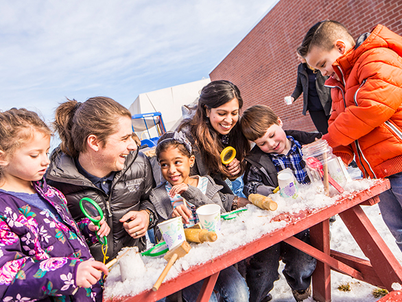 Adults and kids working together at a table while wearing coats and standing outside.